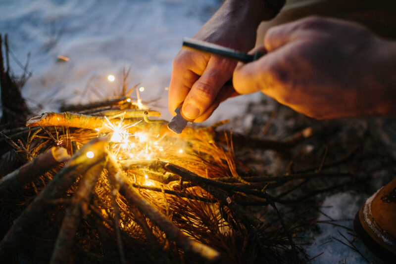 Male hand starts fire with magnesium fire steel, fire striker
